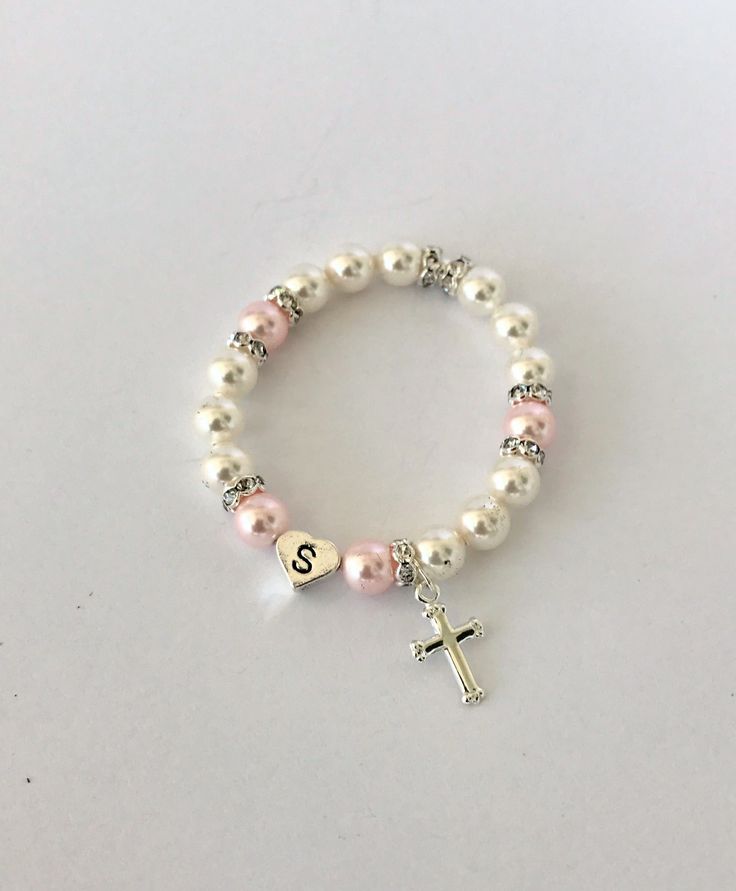 "Gift someone special this timeless gift of a classic pearl bracelet. Swarovski 6mm pearls in white and rosaline circle the wrist and frame a sterling silver heart initial bead. Sparkly rhinestone rondelles add a touch of glitz, and a sterling silver cross hangs by the initial. The bracelet is created on elastic cord for easy on/off. - - - -> WHAT SIZE SHOULD YOU BUY? The listing photo shows a 6 1/2\" bracelet. It's always best to measure a bracelet that currently fits the recipient, but if y Elegant Adjustable Rosary Bracelet For Birthday, Classic Personalized Pearl Bracelet, Personalized Classic Pearl Bracelet, Classic Personalized White Pearl Bracelet, Classic White Bracelets For Mother's Day, Classic White Charm Bracelet As Gift, White Dainty Pearl Bracelet For Birthday, Classic White Charm Bracelet Gift, Pink Pearl Drop Bracelet As Gift