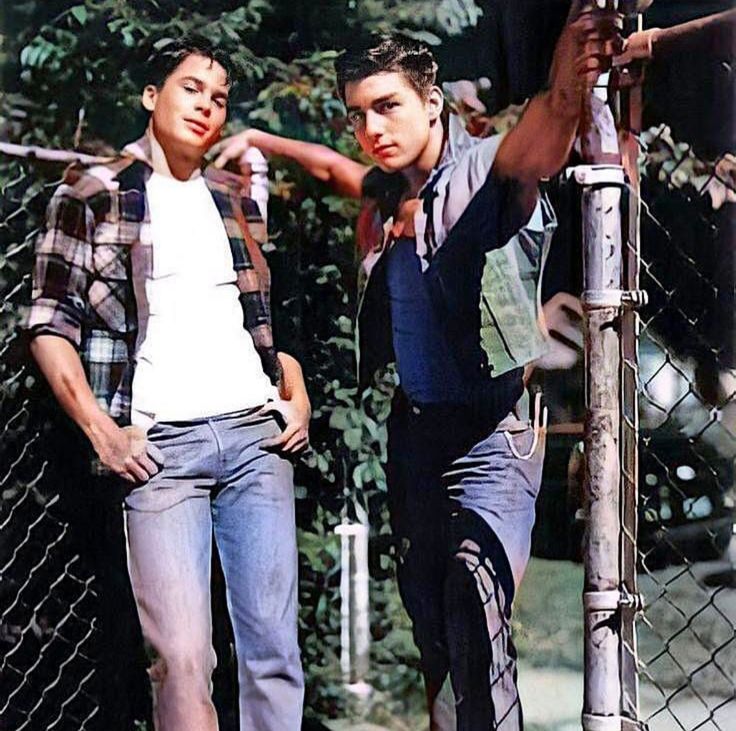 two young men standing next to each other near a fence