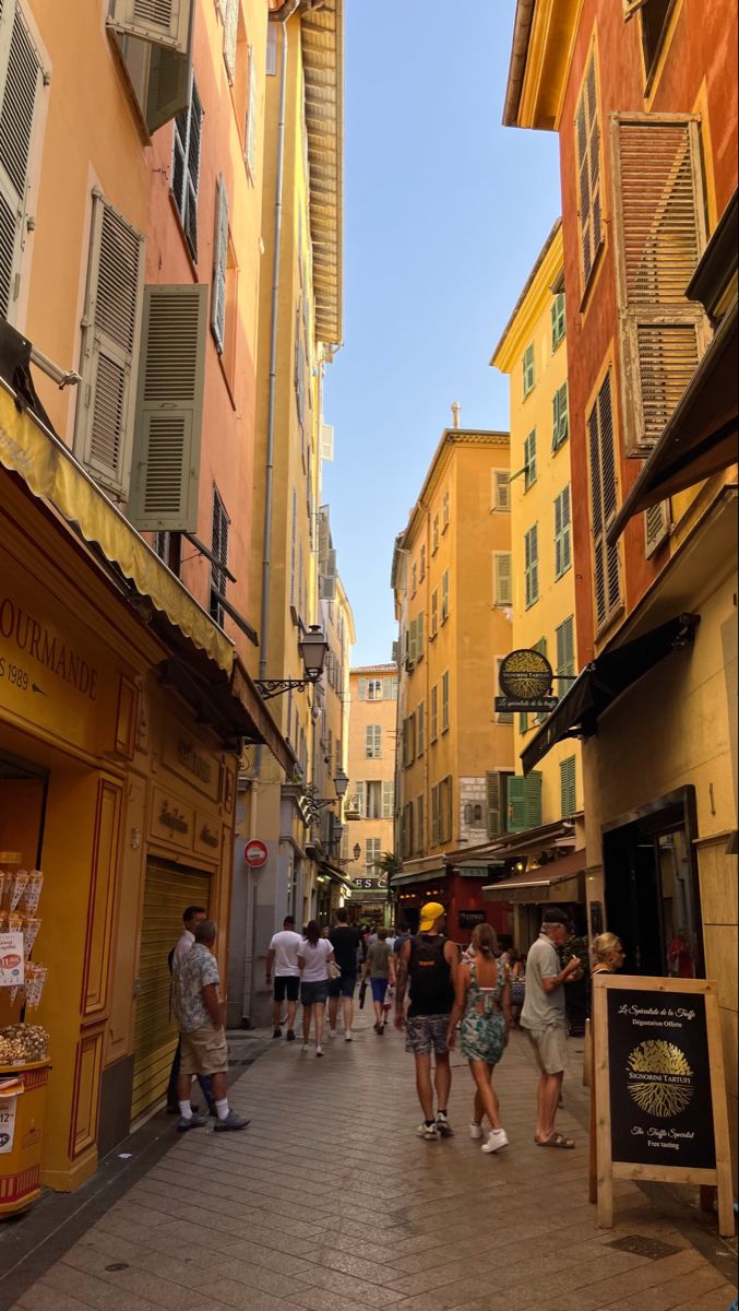 many people are walking down the street in an alleyway with buildings on both sides