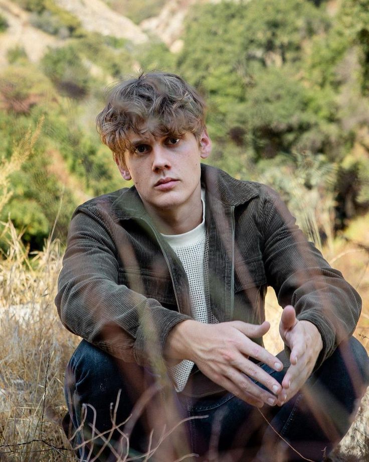 a young man sitting in the grass with his hands on his knees