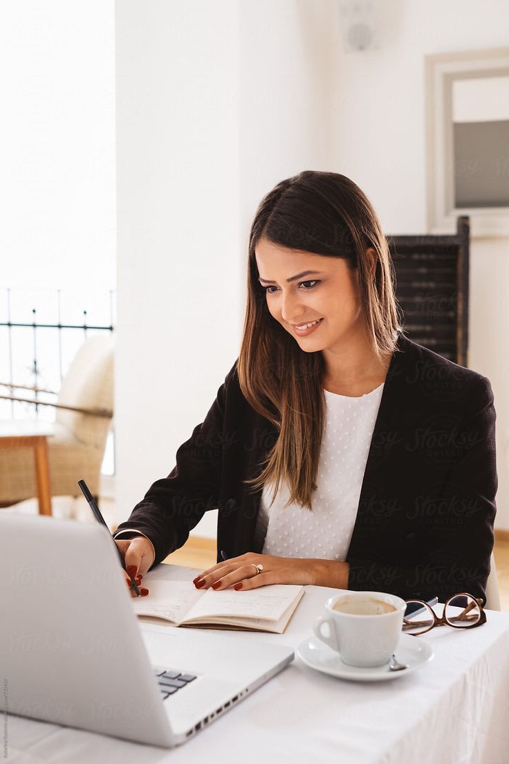 a woman sitting at a table with a laptop and coffee in front of her by an open book