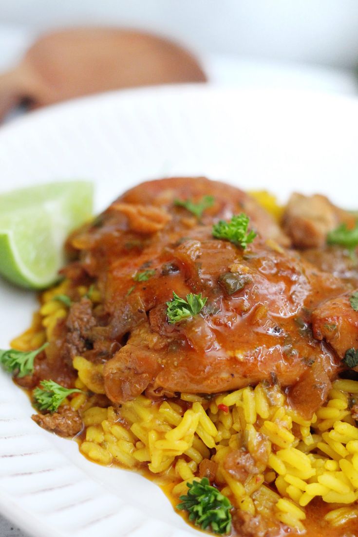 a white plate topped with rice and meat covered in sauce next to a lime wedge