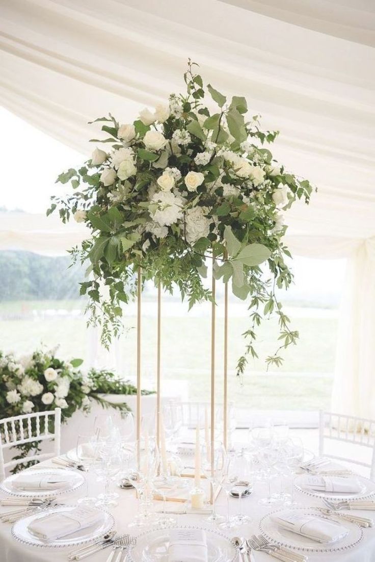 a table with white flowers and greenery on it is set for a formal function