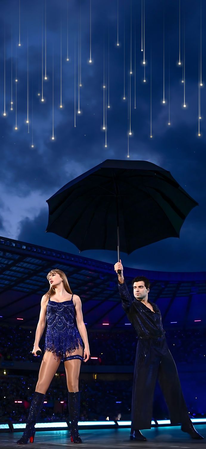 two people standing under an umbrella in the middle of a night time performance at a stadium