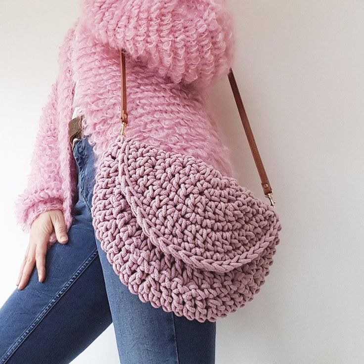 a woman in jeans and a pink sweater is holding a crocheted handbag