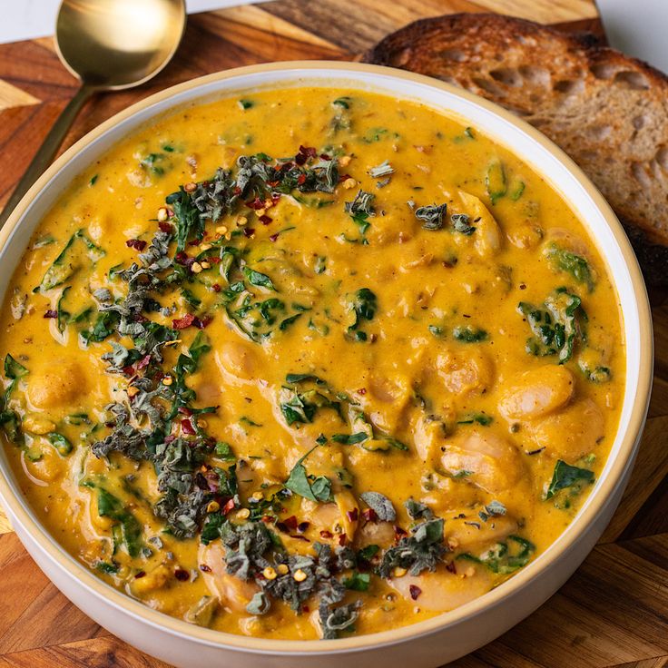 a white bowl filled with yellow soup next to bread on a cutting board and spoon