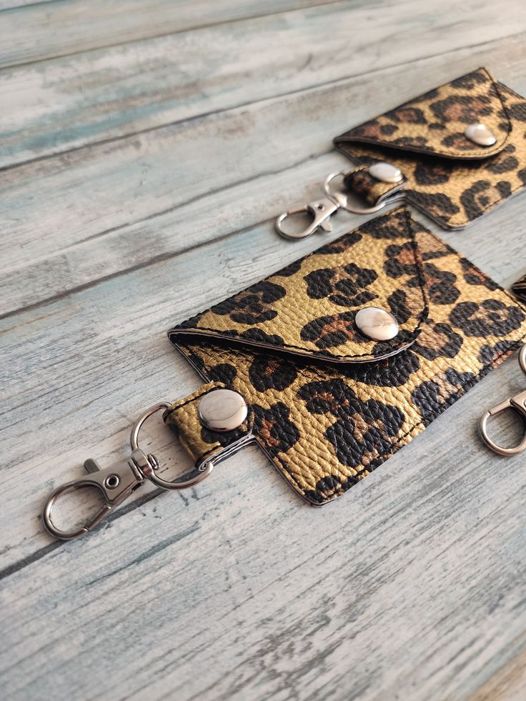 three leopard print wallets with keychains attached to them on a wooden surface