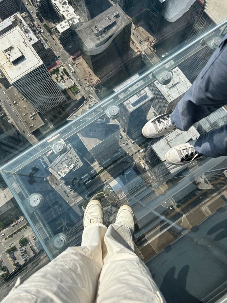 two people standing on the edge of a glass floor with buildings in the back ground