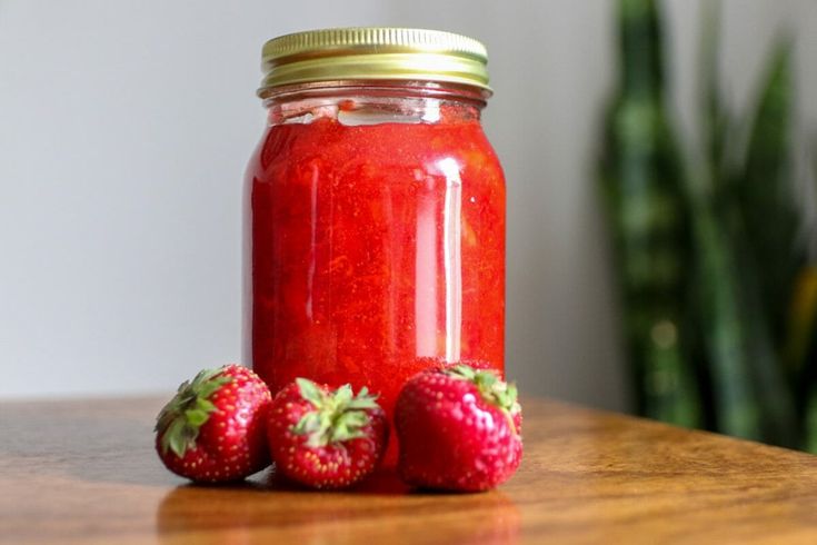 three strawberries sit next to a jar of strawberry jam