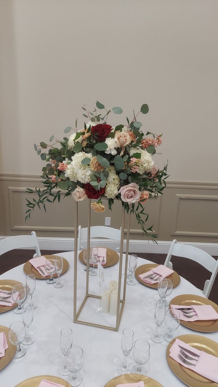 a centerpiece with flowers and greenery sits on a table set for a formal dinner