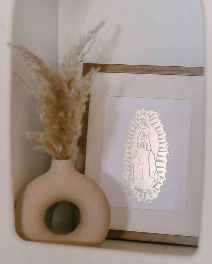 there is a vase with a plant in it next to a framed image and a feather