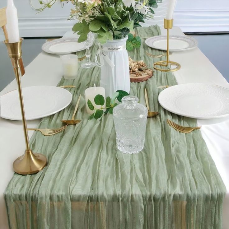 the table is set with white plates and green napkins, gold candles, and flowers