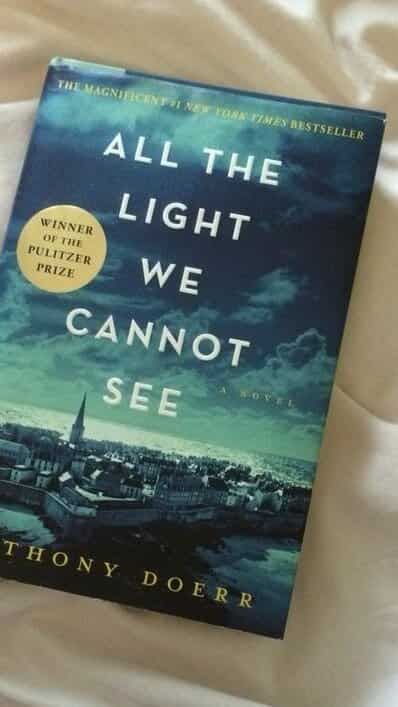 the book all the light we cannot see is laying on a bed