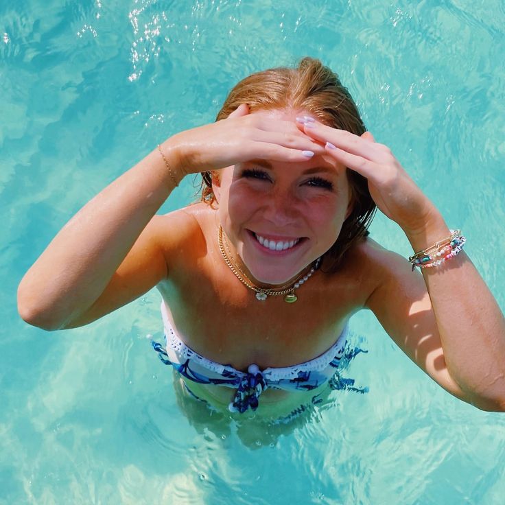 a woman standing in the water with her hands on her head and looking at the camera