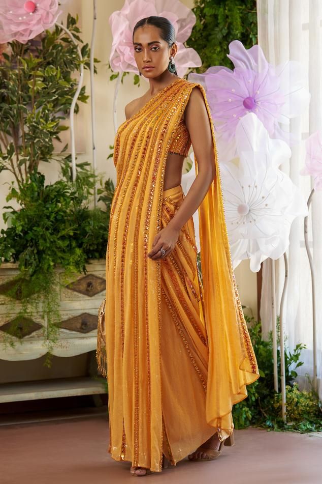 Orange pre-draped saree with all over sequin work, tonal crystal stones, mirror, sequin, beads, cut dana embroidery and attached draped pallu. Paired with one shoulder neck padded blouse with all over embroidery.
Components: 2
Pattern: Embroidered
Type Of Work: Crystal Stones, Thread, Sequin and Bead Work
Neckline: One Shoulder Neck
Sleeve Type: Sleeveless
Fabric: Saree: Sequinned Fabric, Blouse: Butterfly Net
Color: Orange
Other Details: 
Stripe pattern embroidery
Attached lining
Closure:
Saree Evening Pre-draped Saree With Unstitched Blouse For Navratri, Reception Saree With Draped Sleeves And Traditional Drape, Saree With Draped Sleeves For Reception, Reception Saree With Draped Sleeves, Evening Pre-draped Saree In Georgette With Cutdana, Evening Saree With Cutdana For Festivals, Side Open Pre-draped Saree With Dupatta For Party, Evening Saree With Pallu For Navratri, Party Pre-draped Saree With Pallu