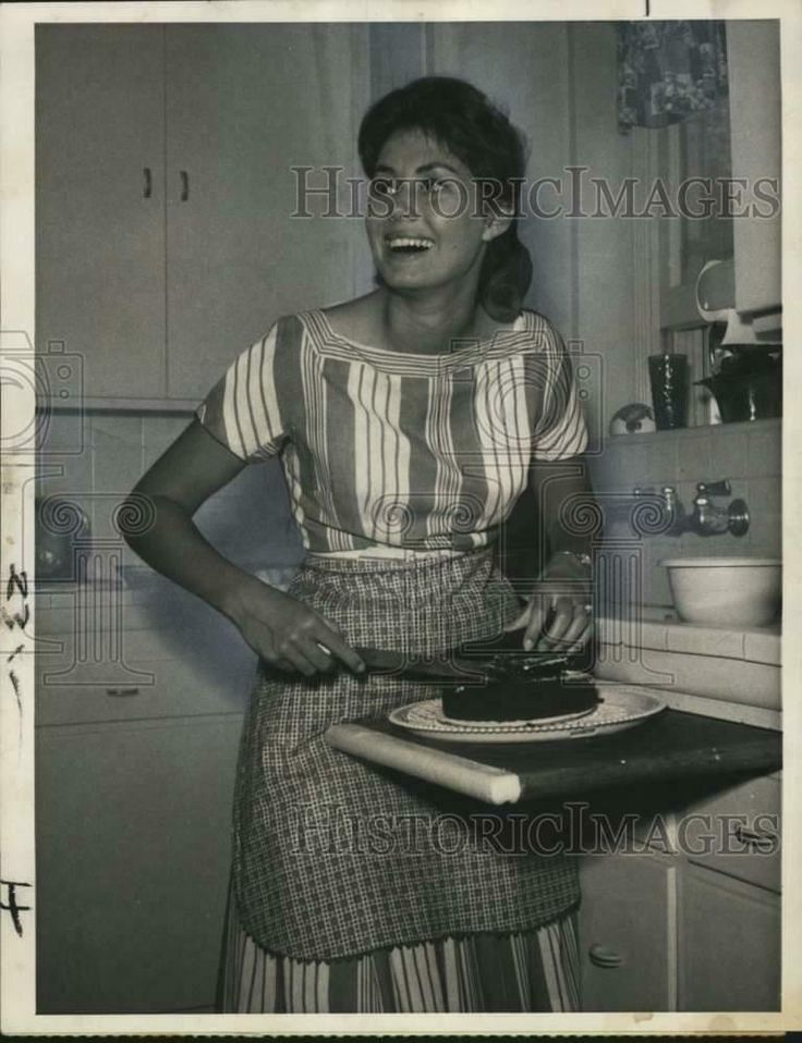 an old black and white photo of a woman in the kitchen with her hand on a pan