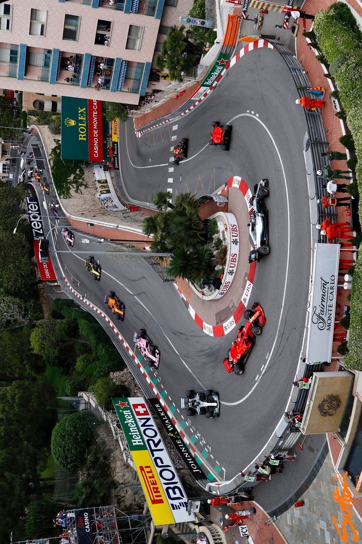 an aerial view of a race track with cars driving on it and buildings in the background