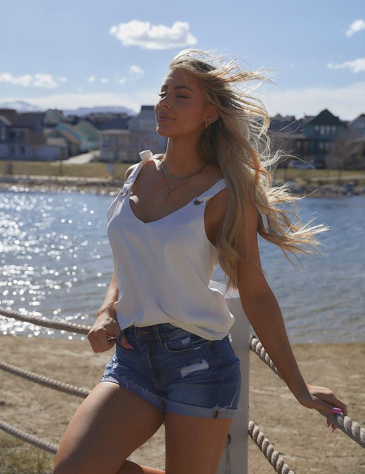 a beautiful young blonde woman leaning on a rope near the water with her hair blowing in the wind