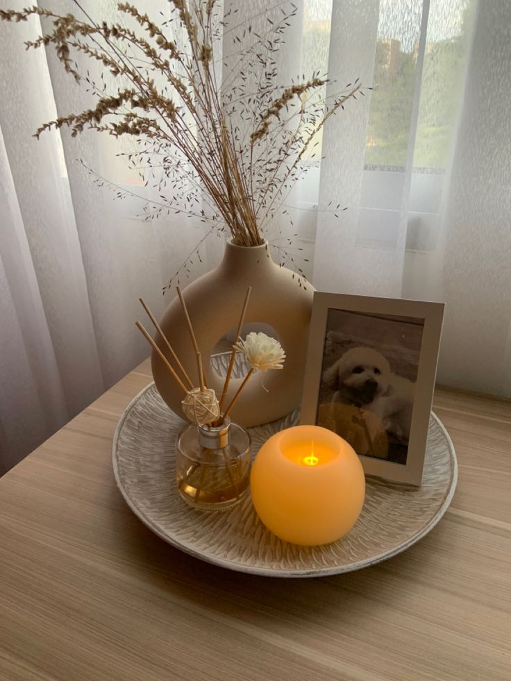 a white plate topped with a vase filled with flowers and a lit candle next to it