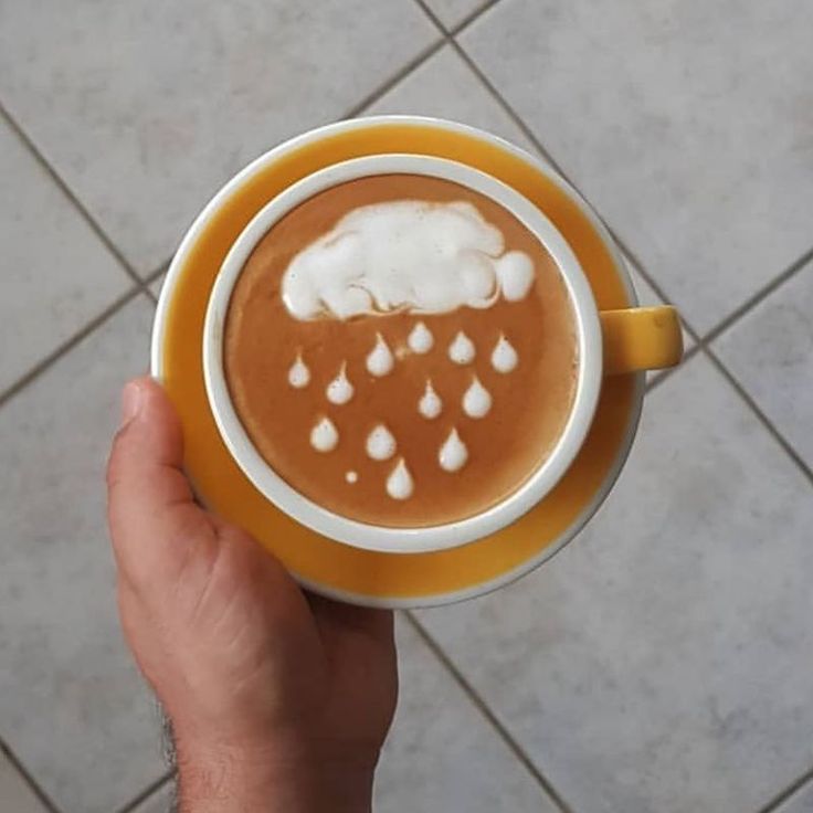 a person holding a cup of hot chocolate with cream in it on a tile floor