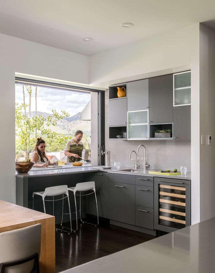 two people are cooking in the kitchen next to an open window that looks out onto mountains