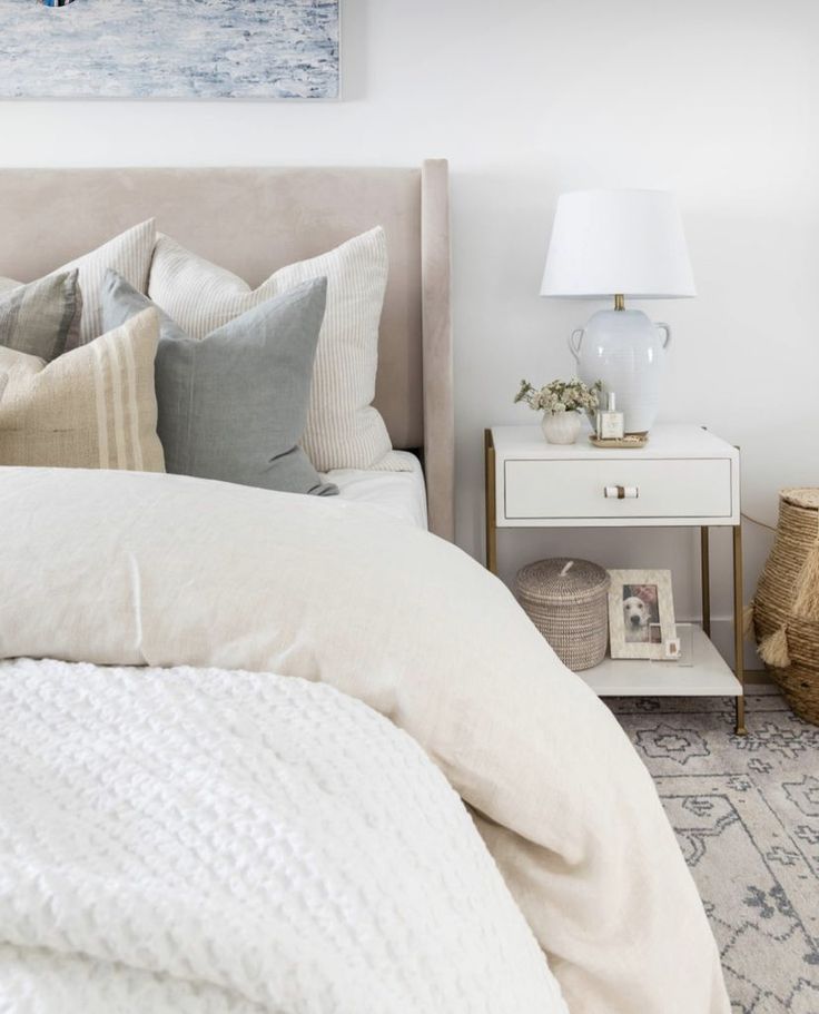 a bed with white linens and pillows in a bedroom next to a painting on the wall