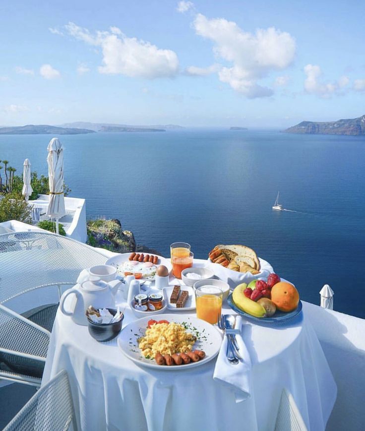 an image of a table with food and drinks on it in front of the ocean