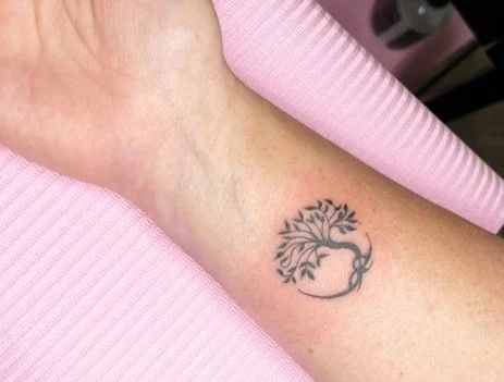 a woman's arm with a small tree tattoo on the left side of her wrist