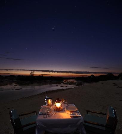 a dinner table set up on the beach at night with candles lit in front of it