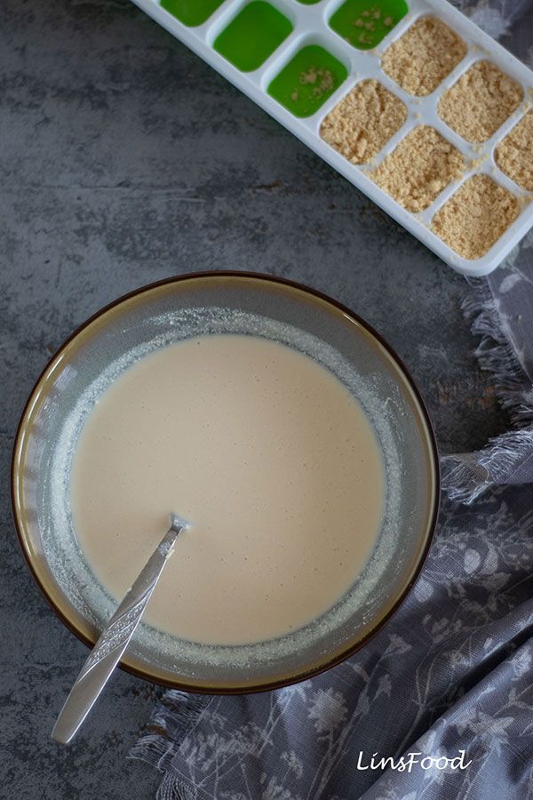 a bowl filled with liquid next to a container of powdered sugar and a spoon