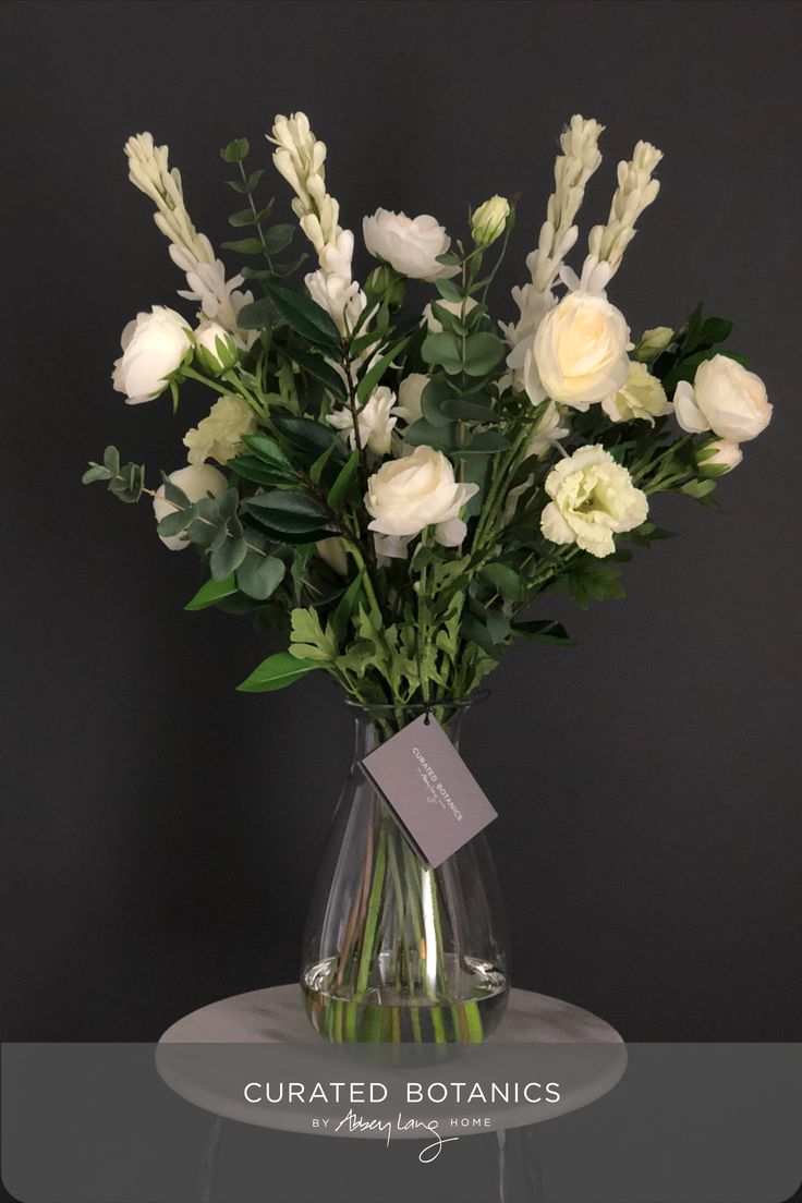 a vase with white flowers and greenery on a glass table, against a black background