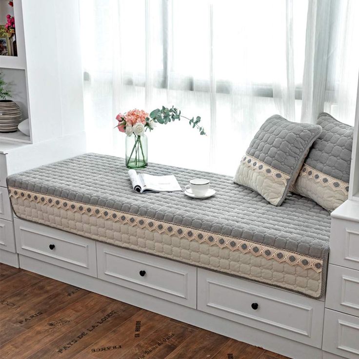 a white daybed with drawers underneath it and a vase filled with flowers on top