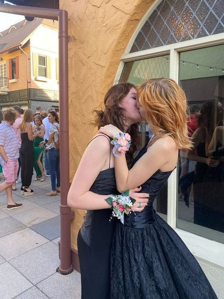 two women are kissing each other in front of a group of people on the sidewalk