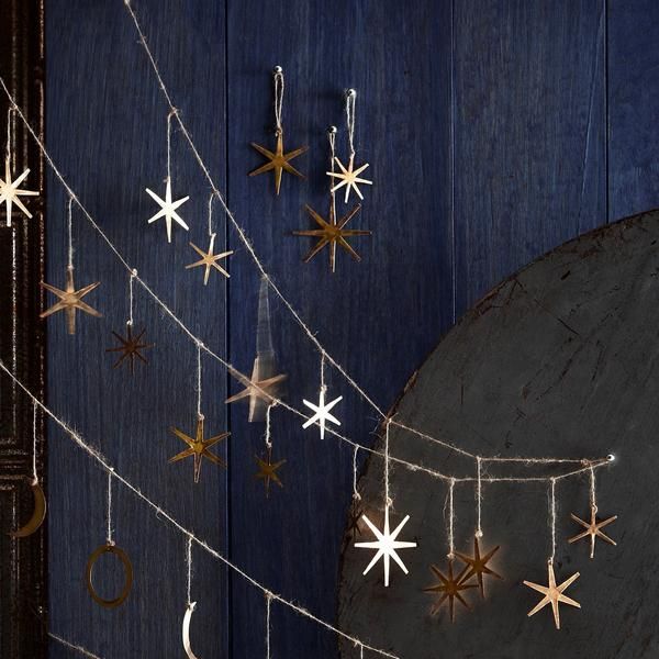 some gold and silver stars hanging from a string on a blue wooden wall next to a round metal object