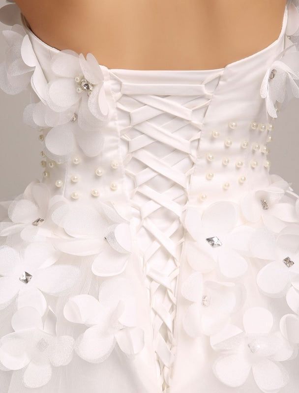 the back of a woman's white wedding dress with flowers and pearls on it