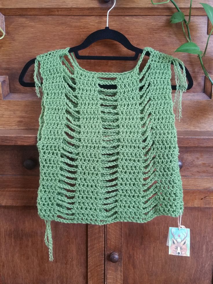 a green crocheted top hanging on a wooden door with a tag attached to it