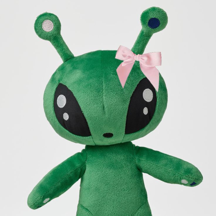 a green stuffed animal with a pink bow on it's head and eyes, sitting in front of a white background