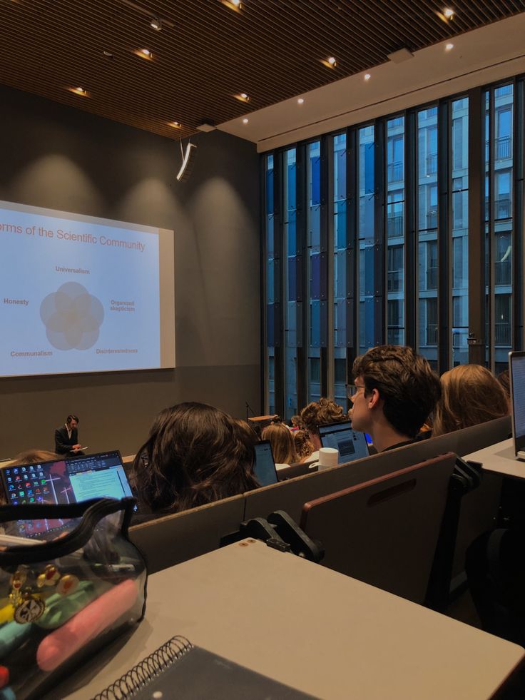 people are sitting at desks with laptops in front of them and a projector screen behind them