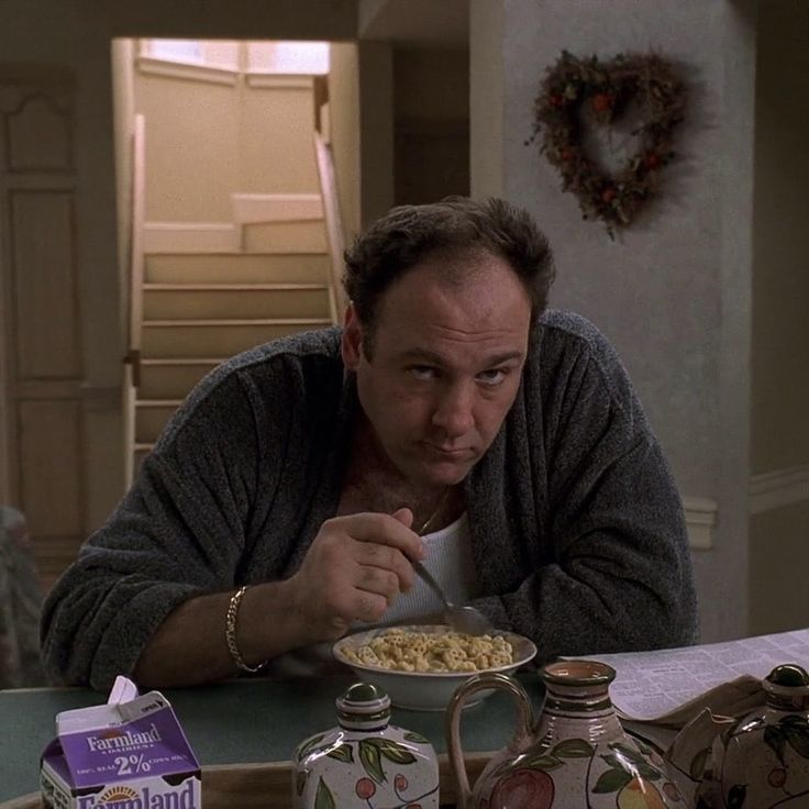 a man sitting at a table eating cereal from a bowl with milk in front of him