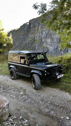 an old black jeep parked on the side of a dirt road in front of a mountain