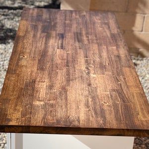 a wooden table sitting on top of a gravel covered ground next to a brick wall