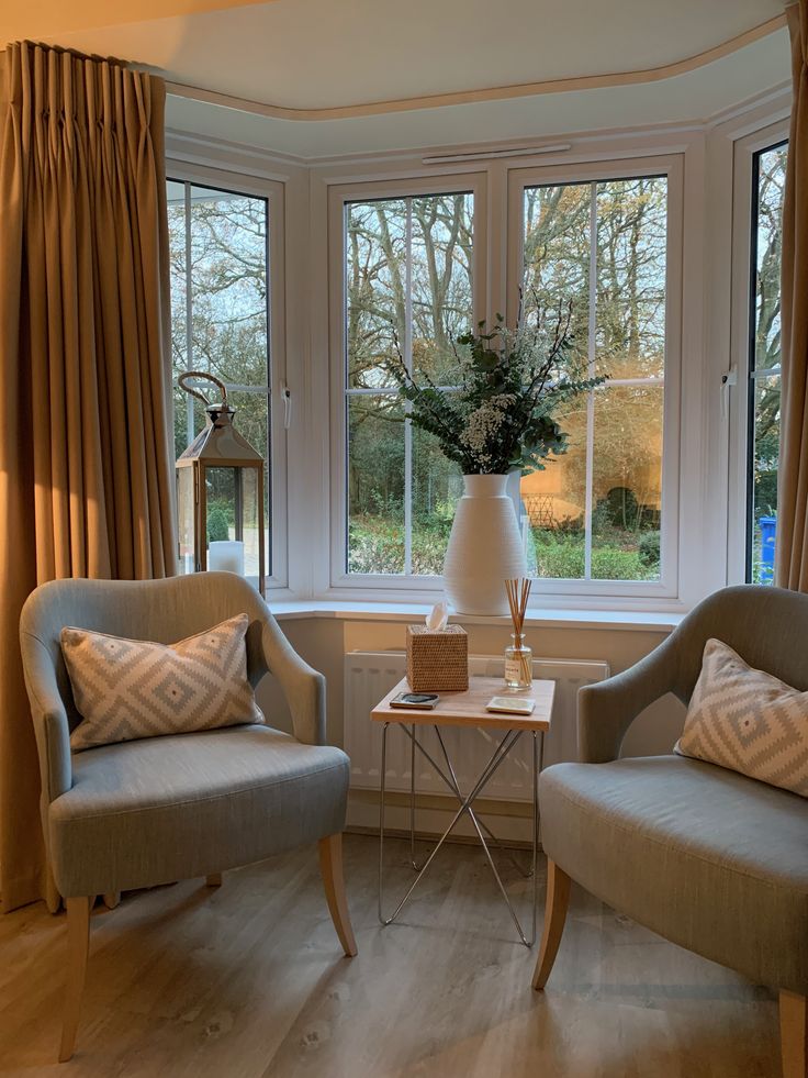 two chairs sitting in front of a window next to a table with a vase on it