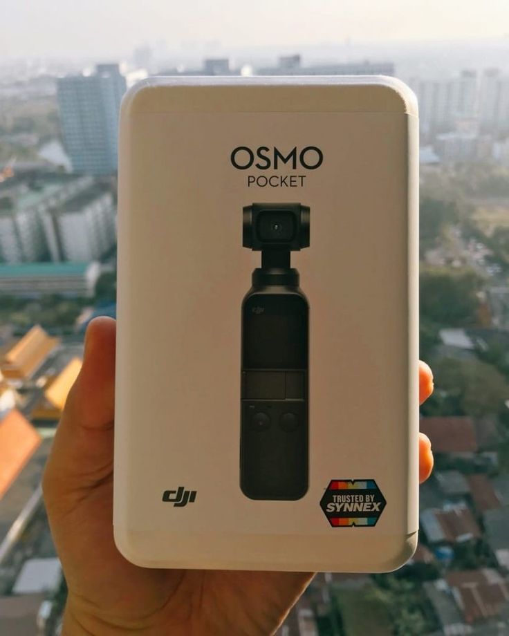 someone is holding up an osmo pocket camera in front of a cityscape