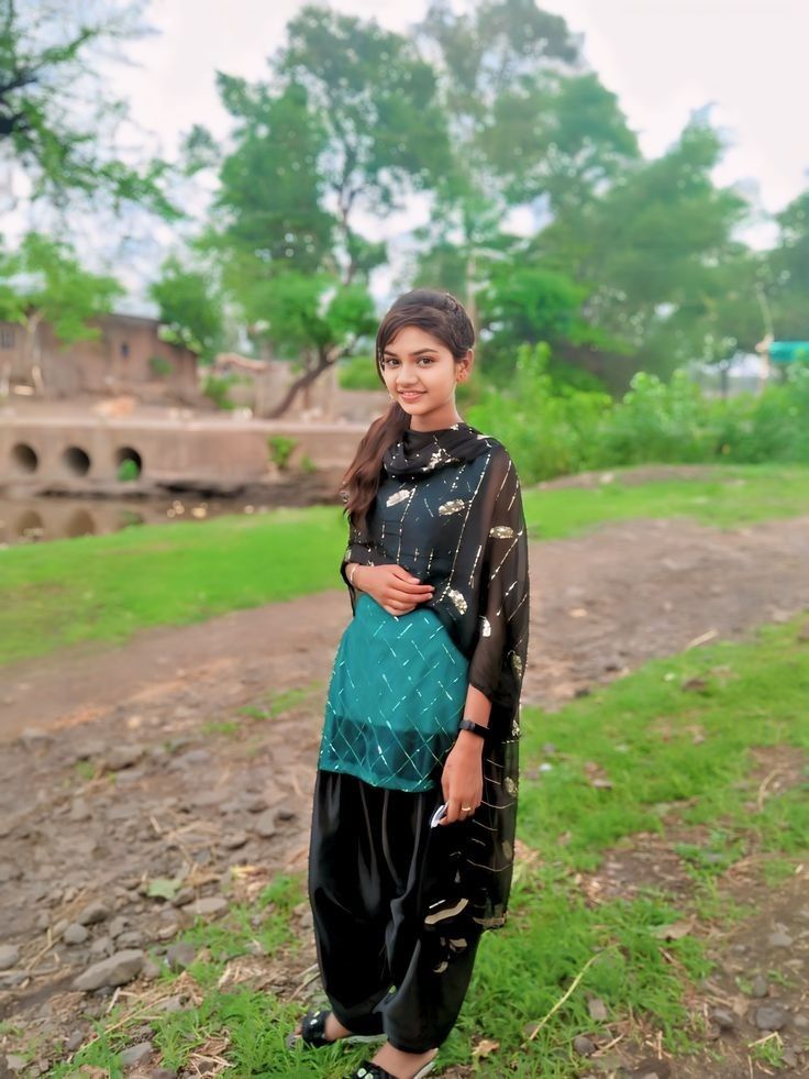 a woman standing on top of a field next to a dirt road and green grass