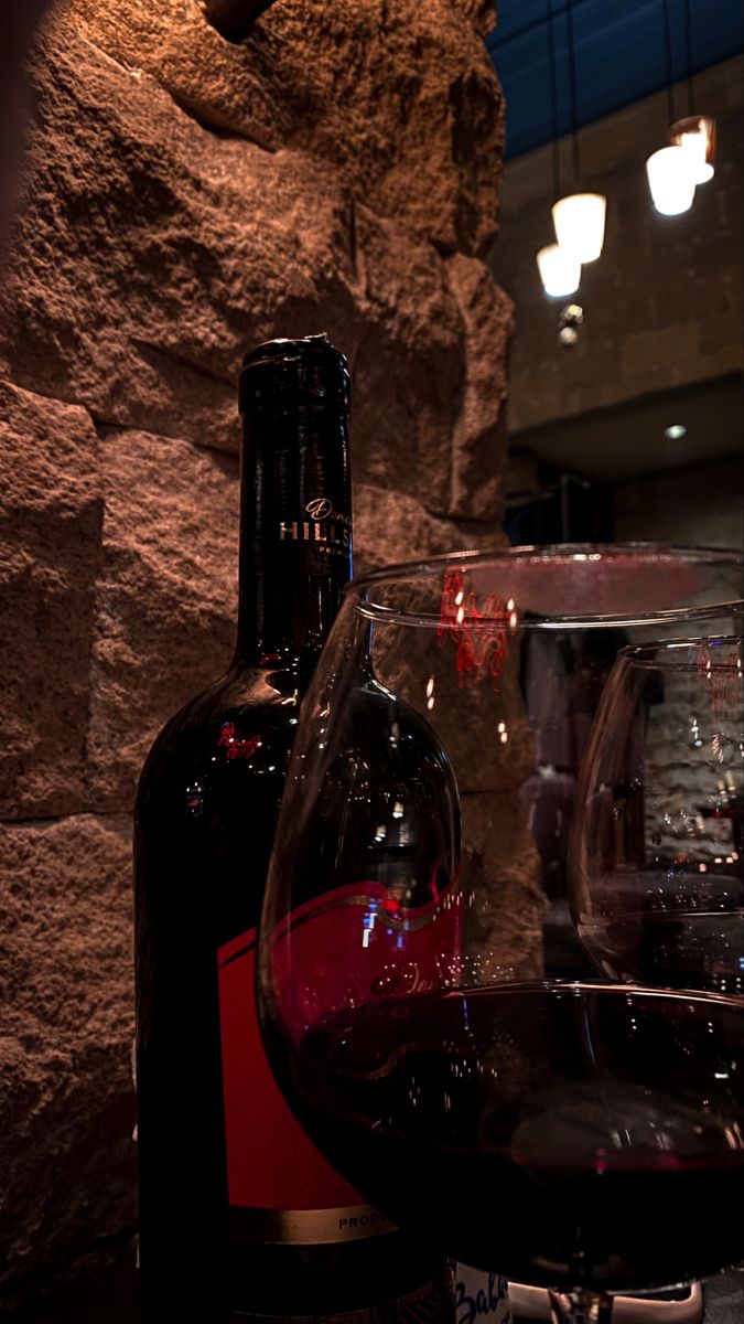 a bottle of wine sitting next to a glass on top of a table with rocks in the background