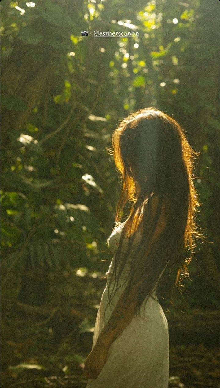 a woman with long hair standing in the woods