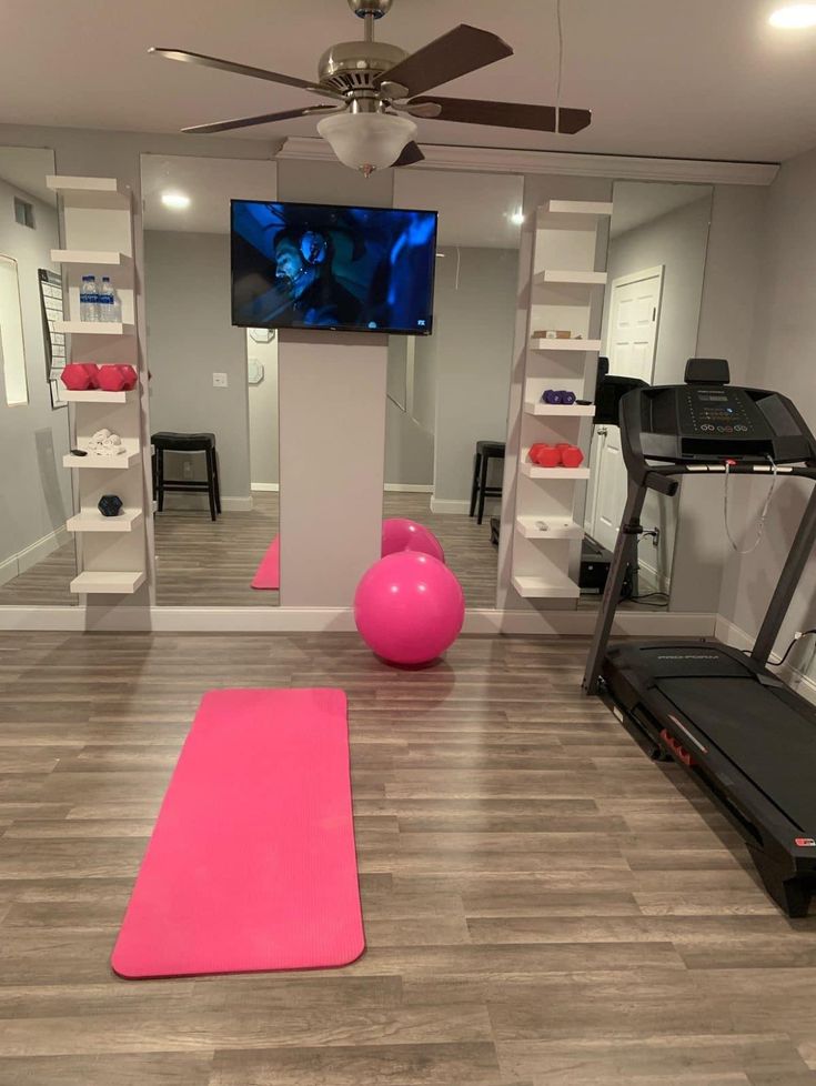 a room with exercise equipment and a television in the corner, as well as pink yoga mats