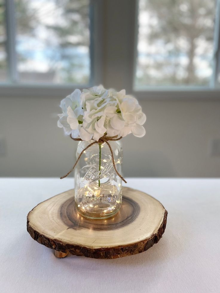 a glass vase with white flowers on a wood slice