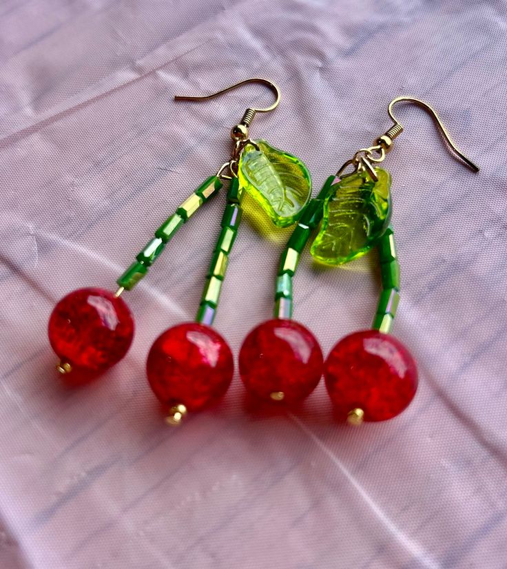 three red cherries with green leaves hang from gold - plated earwires