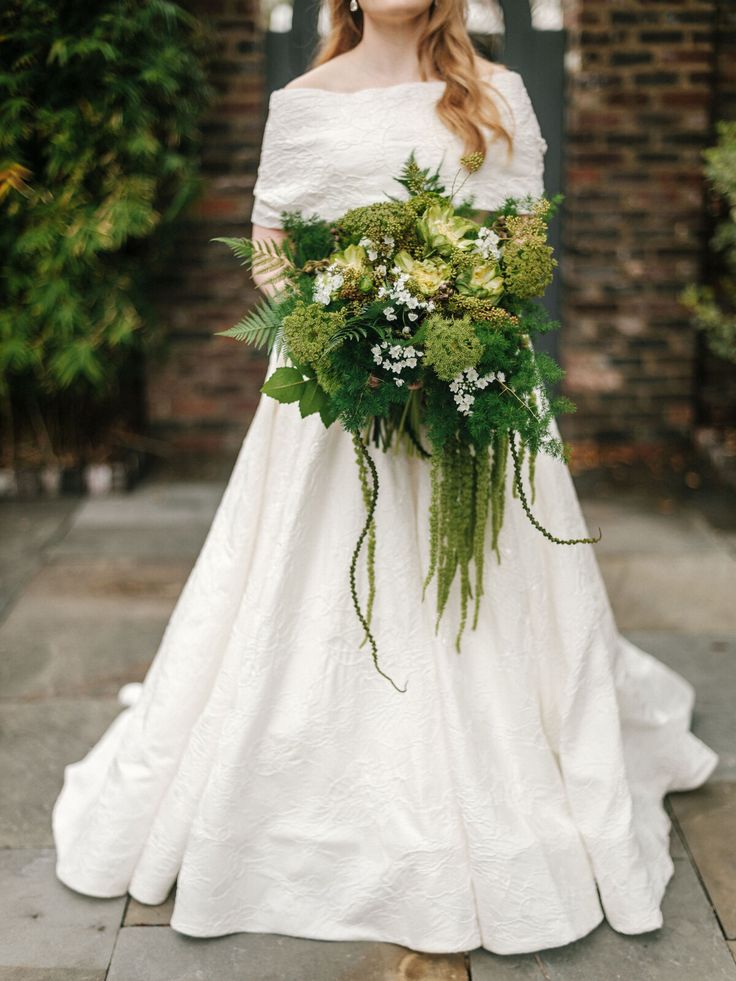 a woman in a white wedding dress holding a bouquet of green flowers and greenery